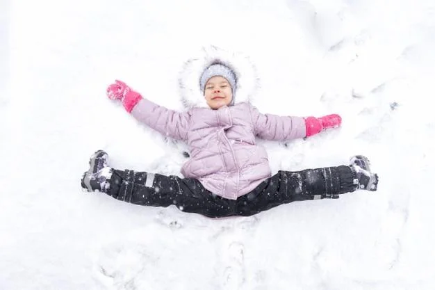 A cute little girl 4 years old in a pink down jacket lies in a snowdrift with a twine and rejoices in the snow. winter fun Premium Photo